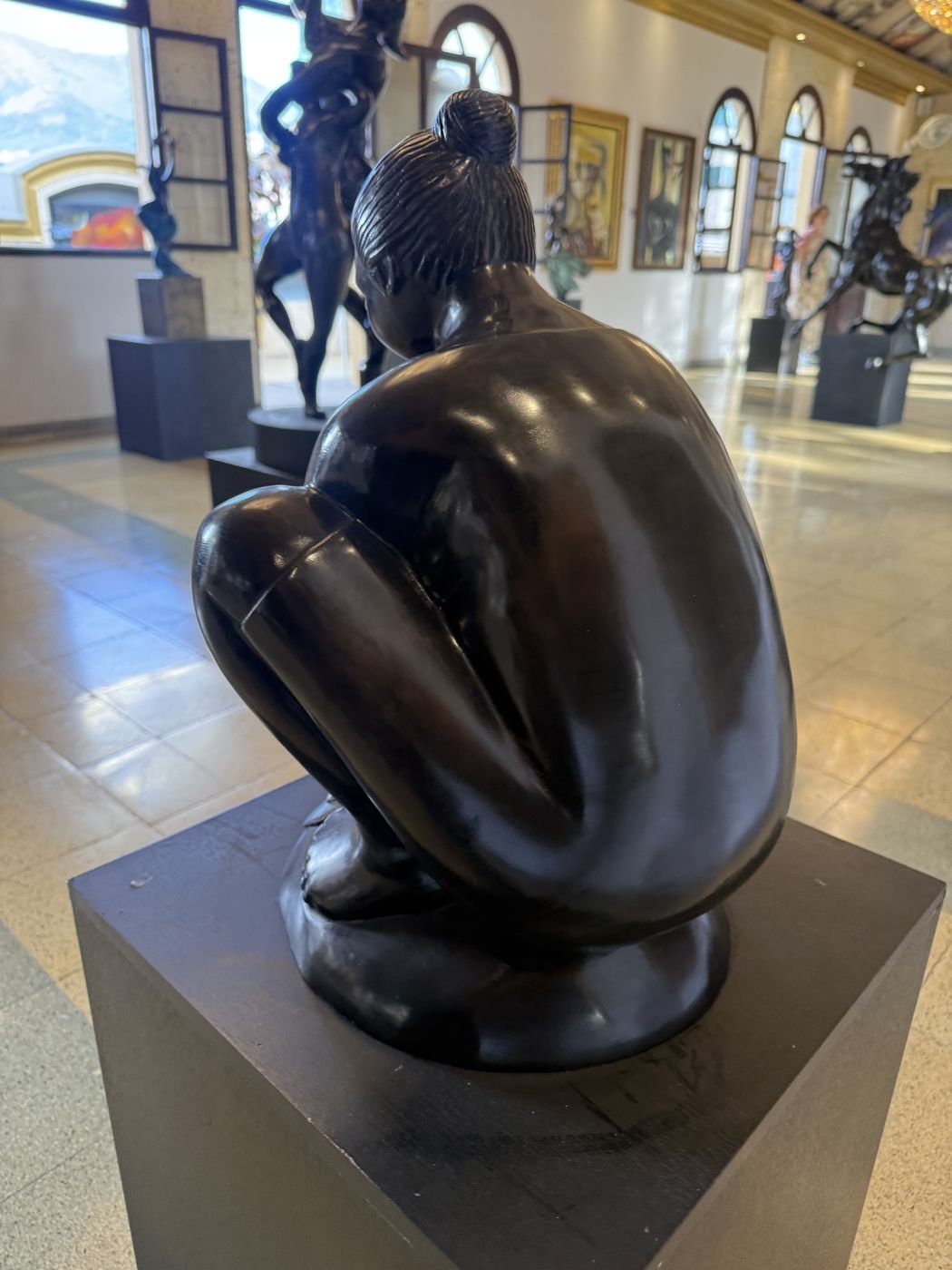A dark bronze of a crouching figure on a black plinth, in the gallery of the Palacio Nacional.