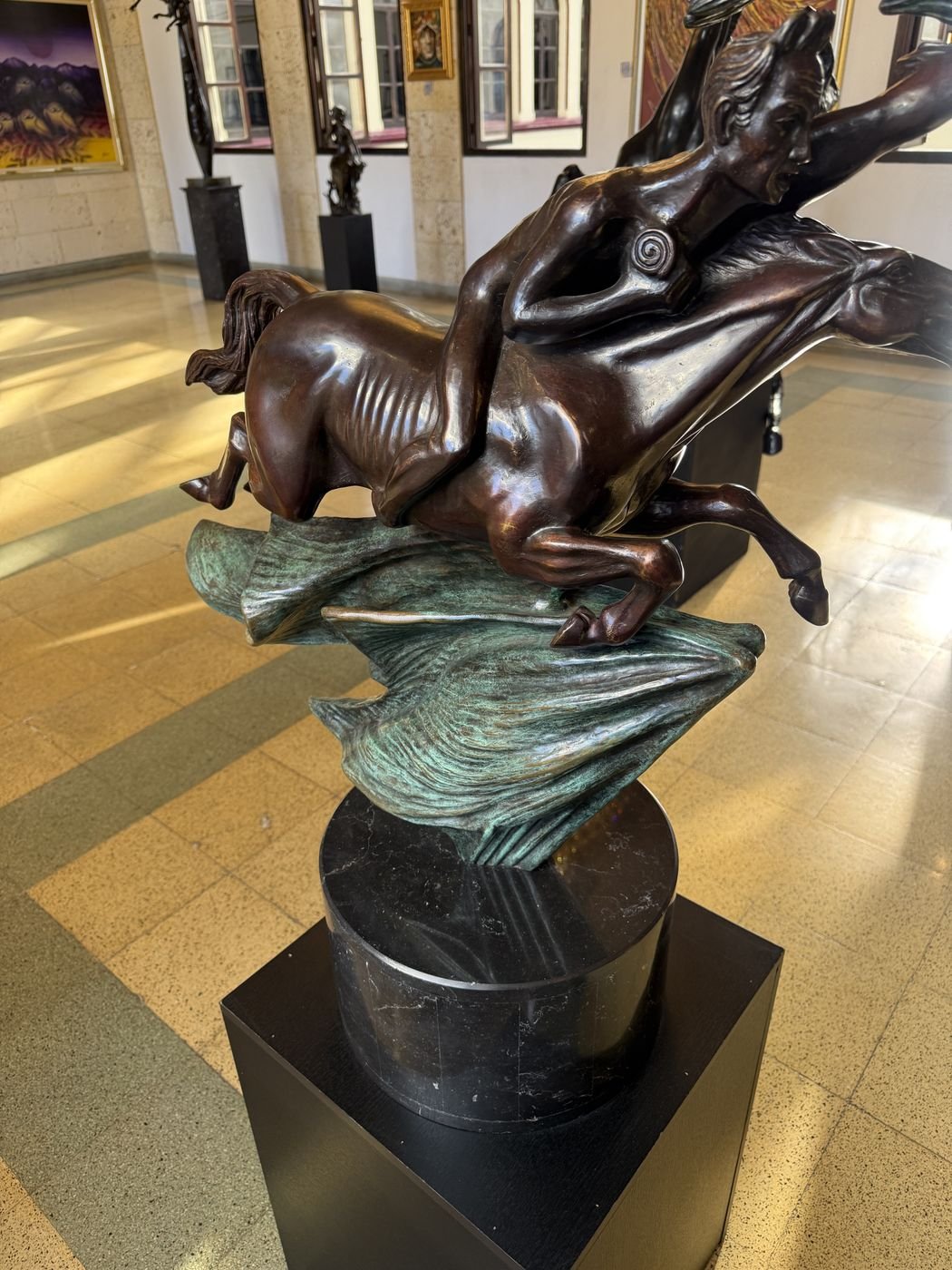 A bronze with green patina, a figure reclining over a horse, on a stone plinth in the gallery.