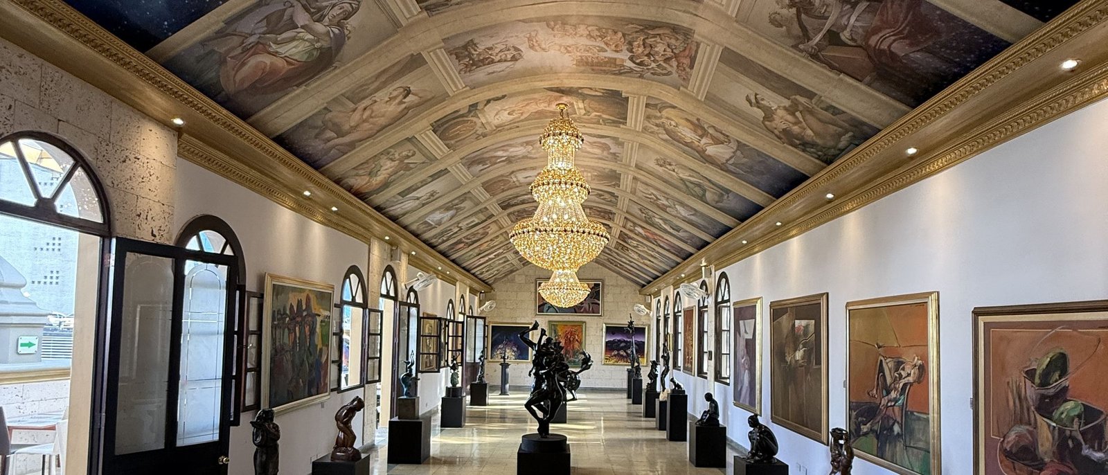 Palacio Nacional, Medellín. The long gallery corridor: a painted vault, a chandelier and sculptures on plinths receding into the distance.