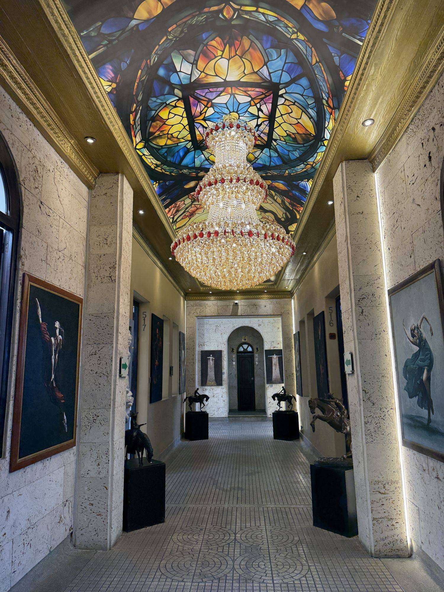 Palacio Nacional, Medellín. The gallery of Galería Cano: a stained-glass dome, a crystal chandelier and bronzes on black plinths along the corridor.